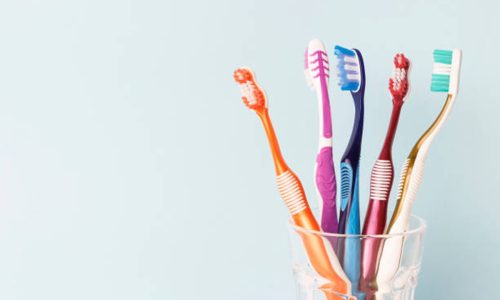 Multi-colored toothbrushes in a glass cup, blue background